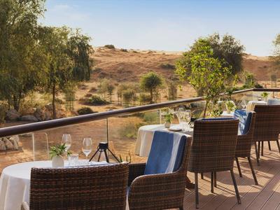 Terrasse mit gedeckten Tischen und Stühlen mit Blick auf eine trockene, bewachsene Landschaft.