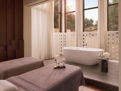 Elegantes Hotelbad mit freistehender Badewanne und zwei Liegen, warme Holzakzente.