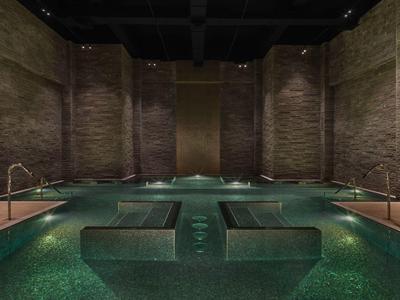 Innenpool mit ruhigem, grünlich beleuchteten Wasser und Ziegelwänden in einem luxuriösen Hotel.