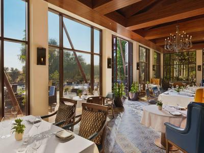 Helles Restaurant mit großen Fenstern, Holzbalken und elegant gedeckten Tischen mit Blick nach draußen.