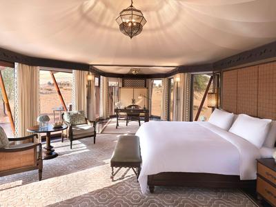 Geräumiges Hotelzimmer mit großem Bett, Sitzbereich und großen Fenstern mit Vorhängen.