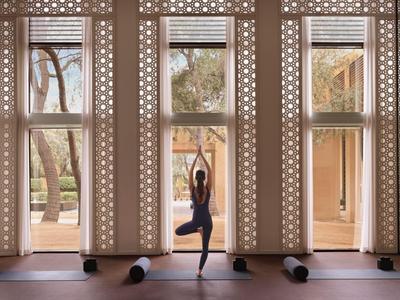 Person übt Yoga in einem hellen Raum mit großen Fenstern und Blick auf einen Garten.