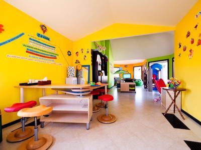Hellgelber Raum mit mehreren Tischen und Stühlen, dekoriert mit bunten Wandmalereien.