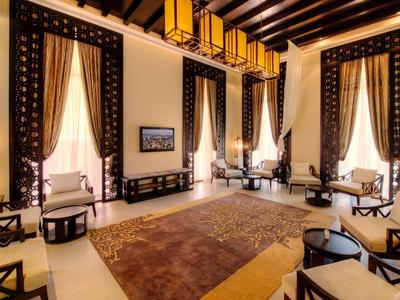 Großer, heller Raum mit hohen Decken, dunklen Vorhängen, hellen Wänden und mehreren Sitzgruppen.