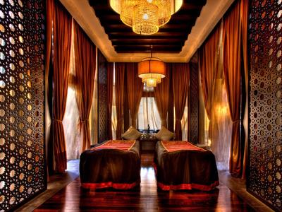 Luxuriöser Raum mit zwei Sesseln, schweren Vorhängen und goldenen Kronleuchtern, warme Farben.