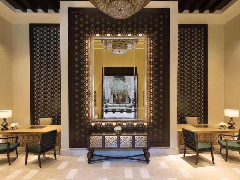 Symmetrischer Raum mit großen Spiegel, zwei Tischen, Stühlen und warmen Beleuchtungselementen.