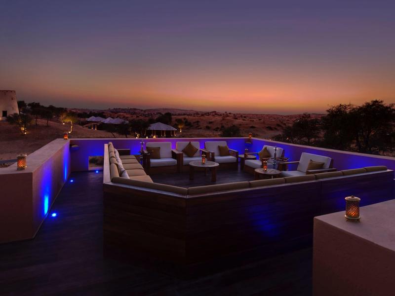 Dachterrasse mit moderner Lounge, blauer Beleuchtung und Sonnenuntergang am Horizont.