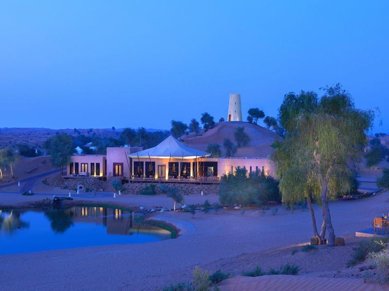 Nachthimmel über einem hell beleuchteten Gebäude neben Wasser mit Sand und grünen Bäumen.