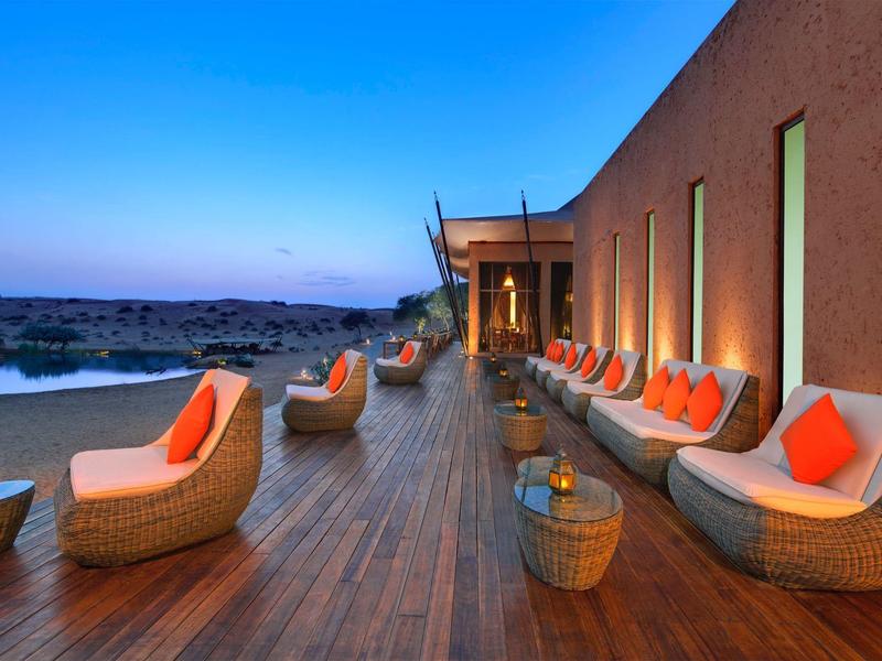 Große Terrasse mit modernen Korbsesseln und orangen Kissen, beleuchtet bei Sonnenuntergang.