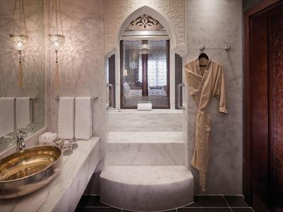 Luxuriöses Badezimmer mit Marmor, goldfarbenem Waschbecken und Bademantel an der Wand.