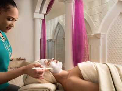 Eine Frau erhält eine Gesichtsbehandlung in einem stilvollen Spa mit hellen Wänden und violetten Vorhängen.