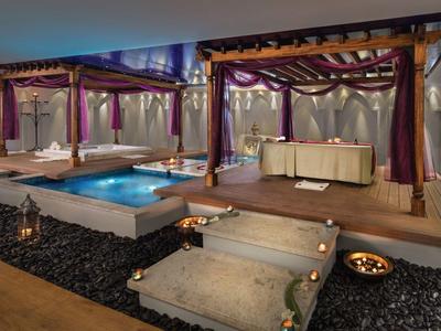 Luxuriöser Außenbereich mit beleuchtetem Pool und Überdachung an einer Hotelterrasse bei Nacht.