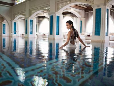 Frau sitzt am Rand eines luxuriösen Hallenbads in einem eleganten Hotel.