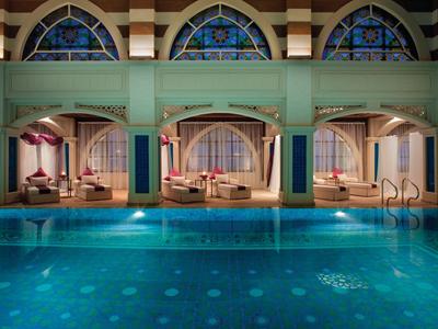 Luxuriöser Poolbereich mit eleganten Tagesbetten und kunstvollen Fensterbögen.