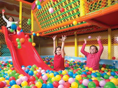 Kinder spielen in einem bunten Bällebad mit Rutsche und Sicherheitsnetz.