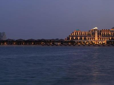 Ein beleuchtetes Hotelgebäude am Ufer bei Nacht mit ruhigem Wasser im Vordergrund.