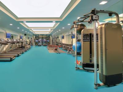 Nowoczesna siłownia z niebieską podłogą, bieżniami i sprzętem do ćwiczeń w jasnym pomieszczeniu.
