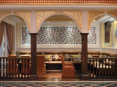 Elegancki hotelowy salon z brązowymi skórzanymi sofami, ozdobnymi kolumnami i żyrandolem.