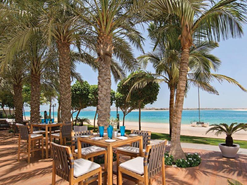 Stühle und Tische unter Palmen mit Blick auf einen Pool und das Meer im Hintergrund.