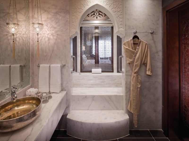 Luxuriöses Badezimmer mit Marmor, goldfarbenem Waschbecken und Bademantel an der Wand.