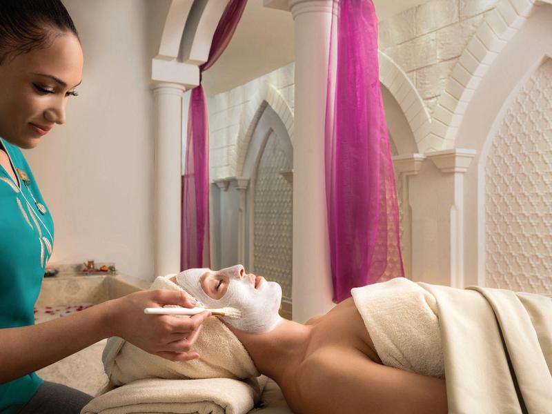 Eine Frau erhält eine Gesichtsbehandlung in einem stilvollen Spa mit hellen Wänden und violetten Vorhängen.