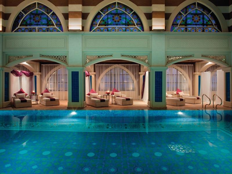 Luxuriöser Poolbereich mit eleganten Tagesbetten und kunstvollen Fensterbögen.