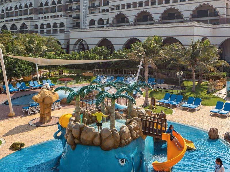 Hotel mit großem Poolbereich, Wasserspielplatz mit Walrutsche und Liegestühlen.