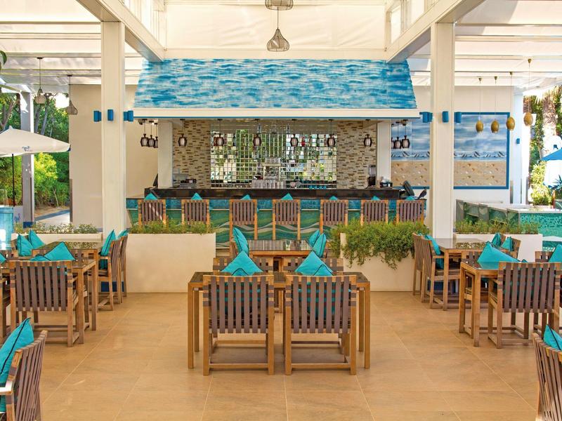 Offene Bar mit Holzmöbeln und türkisfarbenen Akzenten in einem hellen, luftigen Raum.