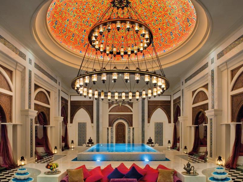 Luxuriöser Innenpool mit aufwendiger Deckenbeleuchtung und gemütlichem Sitzbereich mit bunten Kissen.