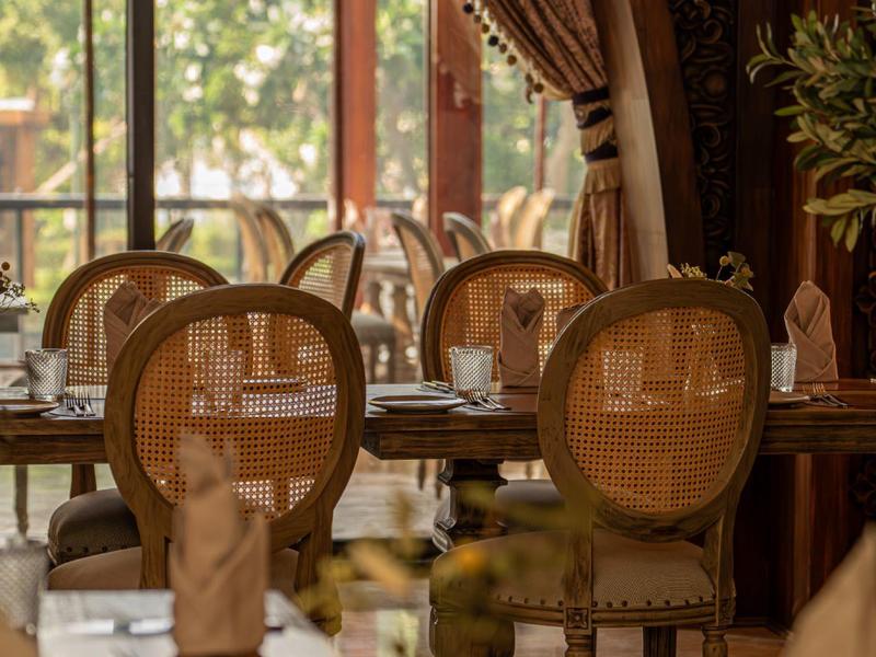 Elegantes Restaurant mit gedeckten Tischen und Stühlen vor großen Fenstern.