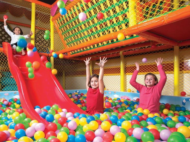 Kinder spielen in einem bunten Bällebad mit Rutsche und Sicherheitsnetz.