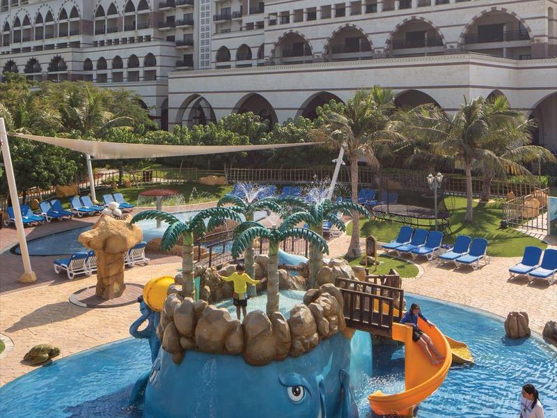 Kinderpool mit blauem Wal-Wasserspiel und Hotelgebäude im Hintergrund