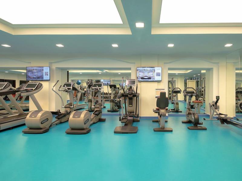 Heller Fitnessraum mit modernen Trainingsgeräten und blauem Boden in einem Hotel.