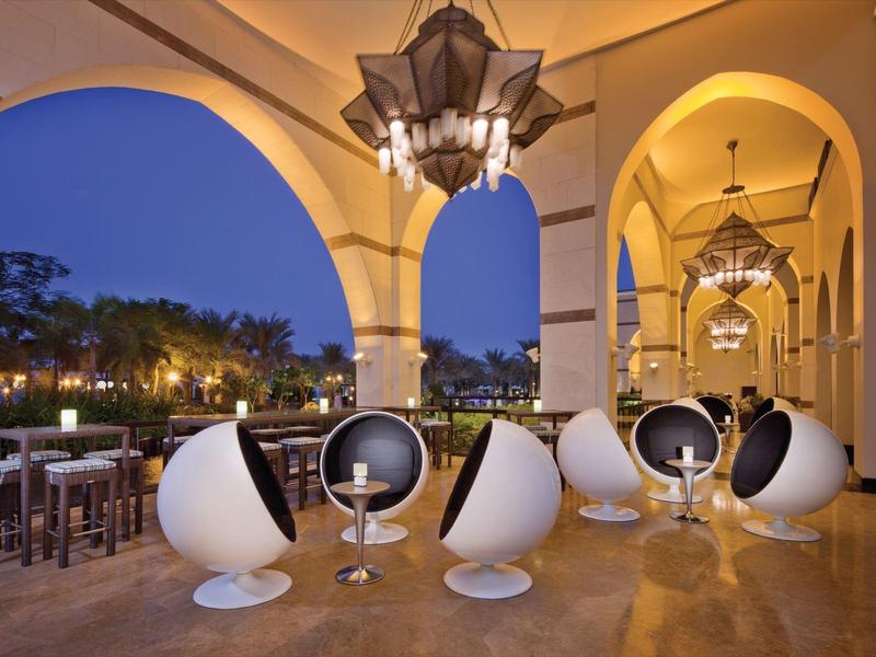 Moderne weiße Kugelsessel und Tische unter einem beleuchteten Arkadengang am Abend.