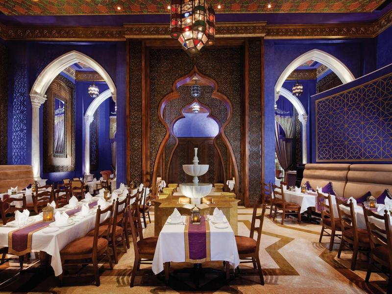 Elegantes Restaurant mit blauen Wänden, Holzdetails und gedeckten Tischen in warmem Licht.