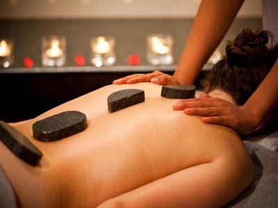 Personne recevant un massage aux pierres chaudes avec des pierres noires sur le dos dans une ambiance relaxante.
