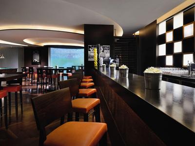 Modern hotel bar with dark wood, illuminated ceiling feature, and orange bar stools.