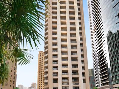 Gratte-ciel moderne avec piscine et palmiers au premier plan sous un ciel clair.