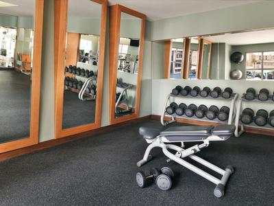 Nowoczesna siłownia z hantlami, regulowaną ławką i dużymi lustrami.