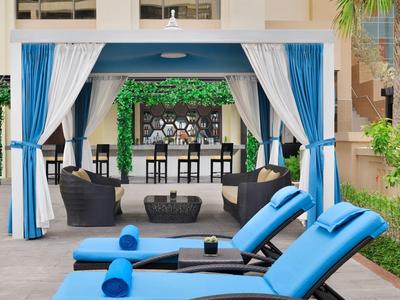 Moderner Außenbereich mit blau-weißer Lounge, Liegestühlen und Bar unter Pergola mit Pflanzen.