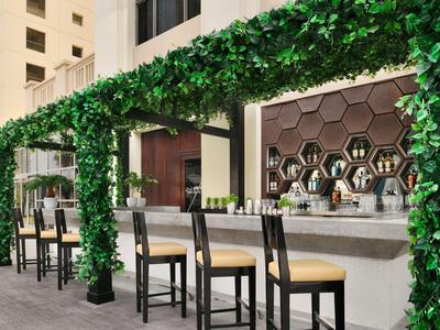 Bar z wysokimi stołkami i zielonym daszkiem z liści w nowoczesnym hotelu.