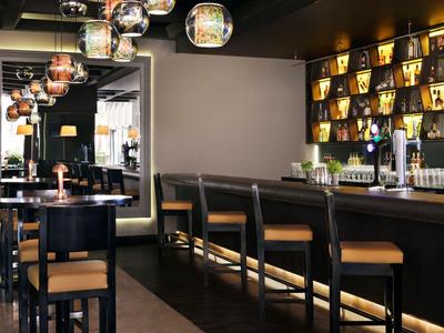 Nowoczesny bar hotelowy z hokerami, oświetleniem nastrojowym i lustrem na ścianie.