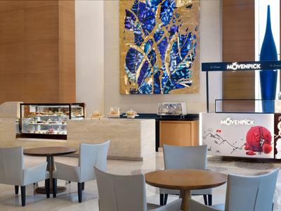 Modern hotel lounge area with wooden tables, gray chairs, and colorful wall art.