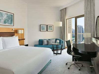 Chambre d'hôtel moderne avec lit double, bureau, chaise et grande fenêtre avec vue sur la ville.