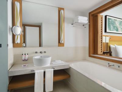 Salle de bain d'hôtel moderne avec baignoire, lavabo et grand miroir aux tons chauds.
