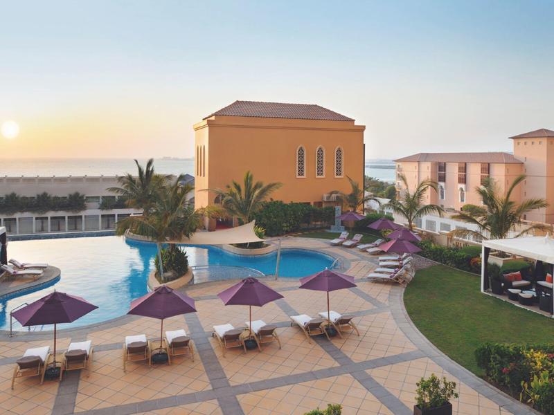 Vue sur une piscine d'hôtel avec transats et parasols au coucher du soleil