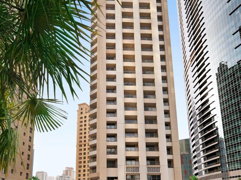 Gratte-ciel moderne avec piscine et palmiers au premier plan sous un ciel clair.