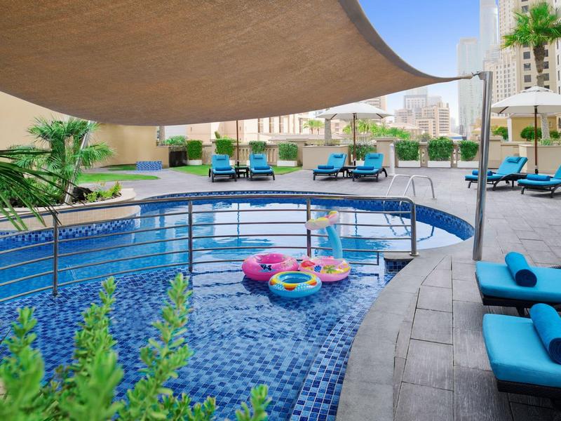Piscine d'hôtel avec transats bleus et bouées colorées sous un ciel clair.