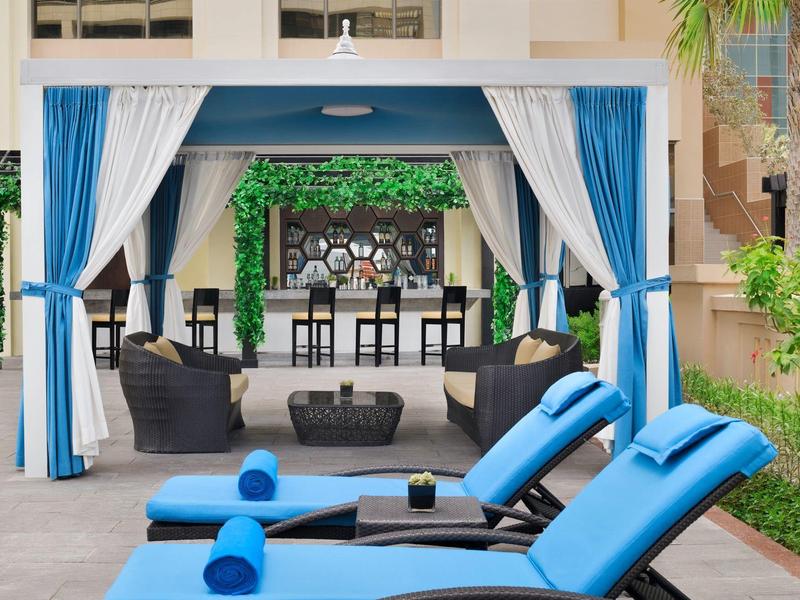 Coin salon extérieur confortable avec rideaux bleu et blanc et chaises longues près de la piscine.