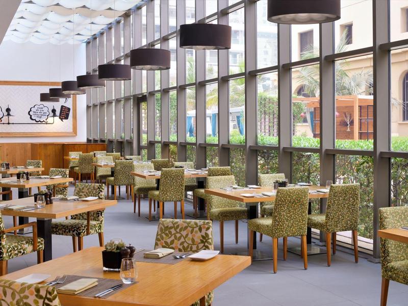 Restaurant d'hôtel lumineux avec grandes fenêtres, chaises vertes et tables en bois.